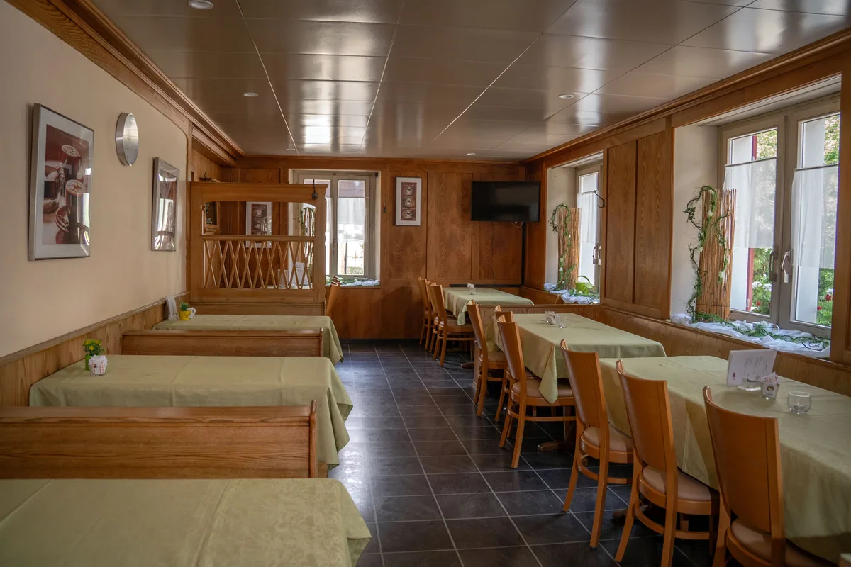 Blick in ein Restaurant. Man sieht grün gedeckte Tische in einem rustikalen Raum.